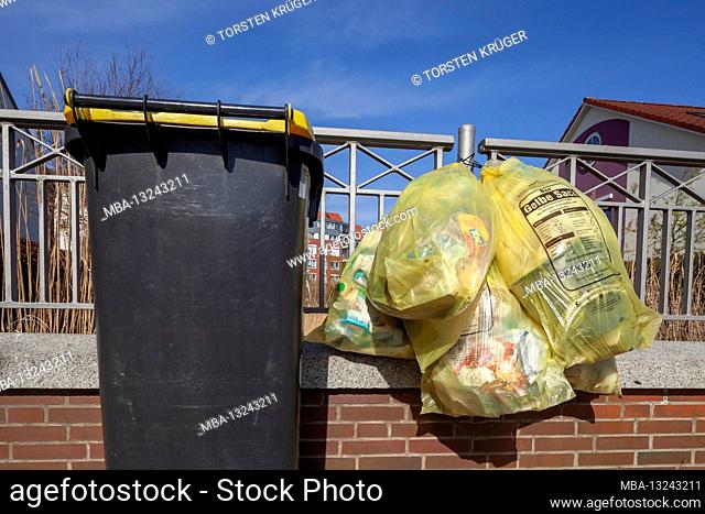 Yellow bin and yellow bags for plastic waste, hanging on a garden fence, Germany