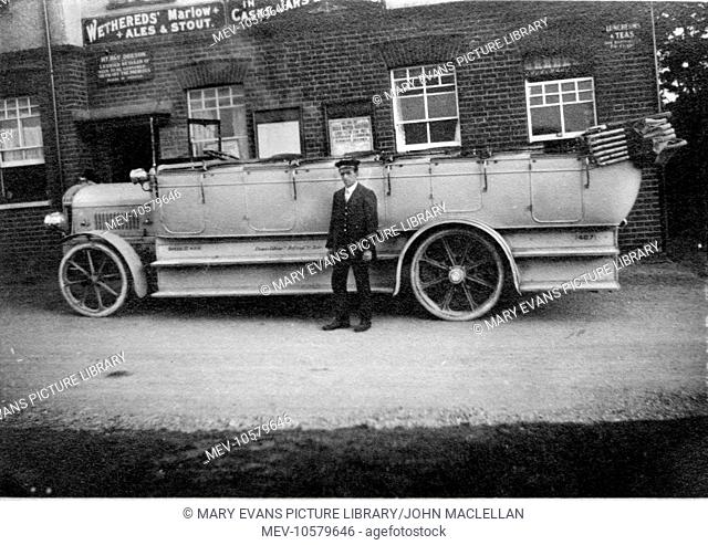 Driver standing in front of his charabanc outside a pub