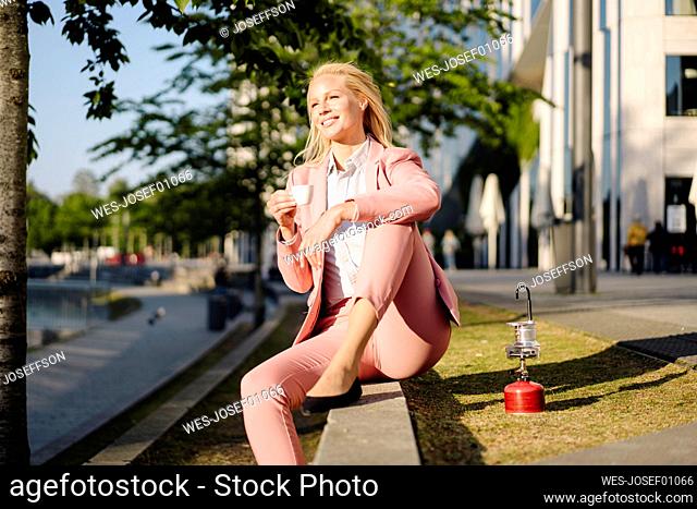 Smiling female entrepreneur looking away while holding coffee cup by camping stove in city