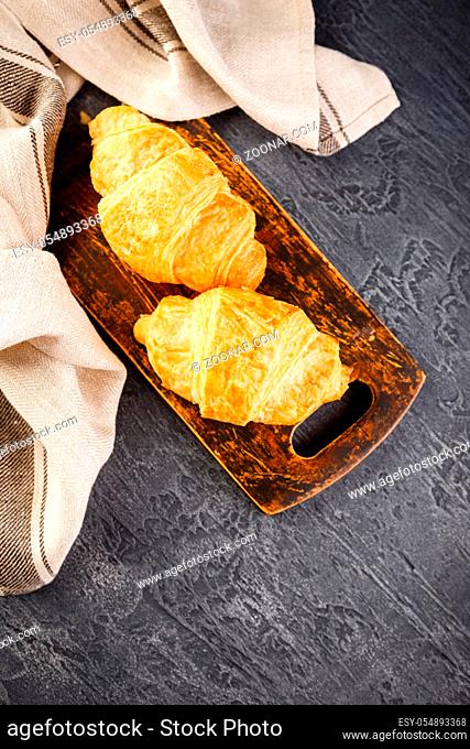 Tasty freshly baked croissants on wooden cutting board, top view
