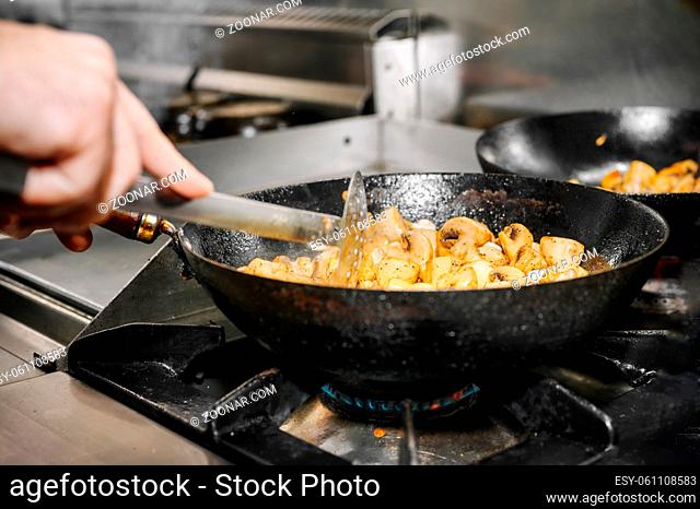 Chef cooking mushrooms in frying pan on burning fire. High quality image