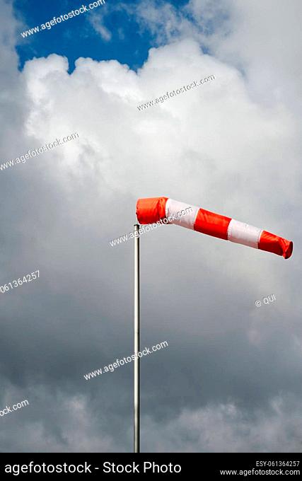 red windsock/ textile tube on a stormy sky at daytime, daylight, dark clouds with the sun breaking through