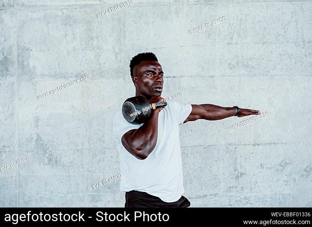 Young male athlete exercising with kettle bell against white wall