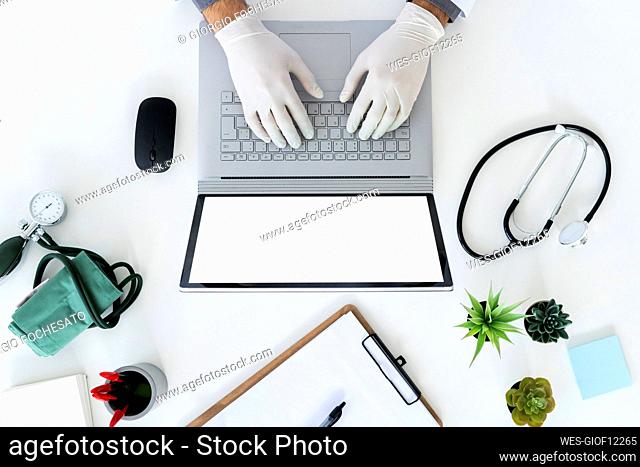 Male doctor wearing surgical glove typing on laptop