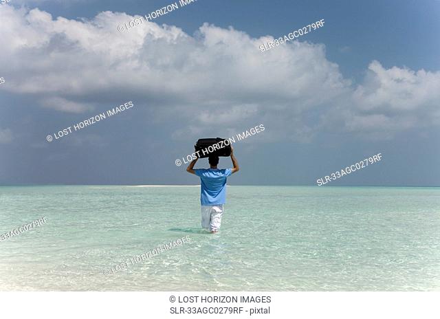 Man carrying luggage into water at beach