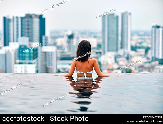 Back view of slim beautiful woman relax in swimming pool. Summer vacation concept