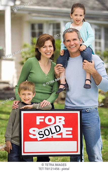 Family in front of house with For Sale/Sold sign