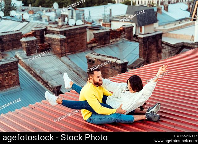 Loving young couple is sitting on the roof of the house. In the background of a big city house