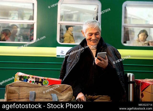 The old man at the train station platform using a mobile phone