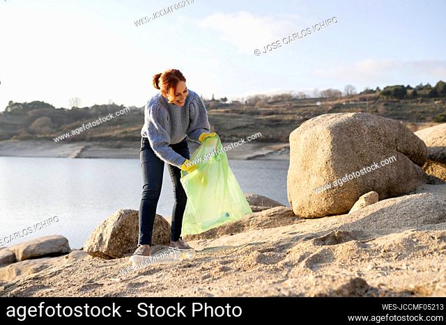 Smiling woman collecting plastic waste by seashore