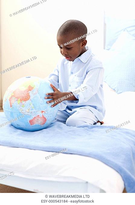 Little boy holding a terrestrial globe lying on his bed