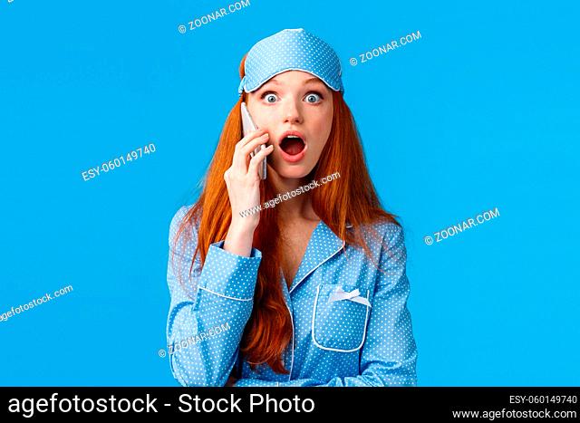 Amazed girl found out shocking news as talking friend on phone. Shocked and astonished startled young redhead woman in sleep mask and pyjama stare impressed