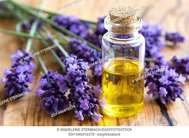 A bottle of essential oil with fresh lavender twigs on a wooden background