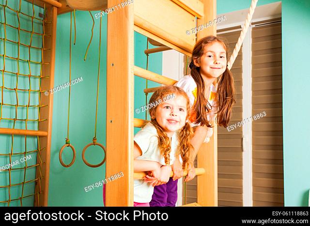 Two cute cheerful kids having fun on rope-ladder climbing and swingigng on it. Siblings strengthen themselves at home wooden sport complex