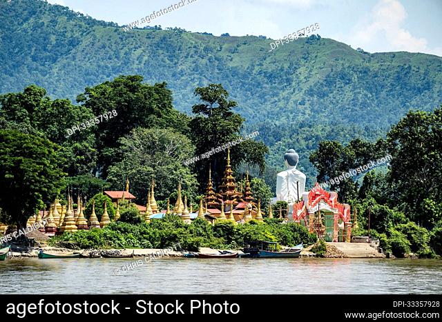 View from Behind of a Giant Buddha beside pagodas and golden stupas on Shwe Paw Island and boats moored along the Ayeyarwady (Irrawaddy) River; Shwegu, Kachin