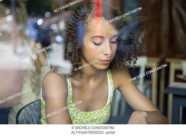 Young woman viewed through window, looking down in thought