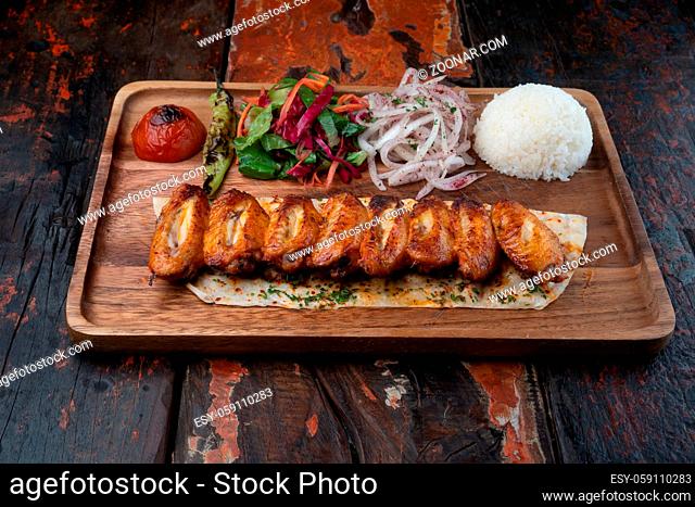 Turkish chicken wings kebab with rice and vegetables isolated on rustic wooden table