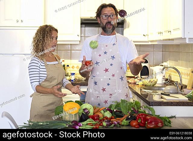 Mature young adult man and woman play and have fun in the kitchen during lunch preparation with fresh vegetables. Happy couple of people enjoy time together at...