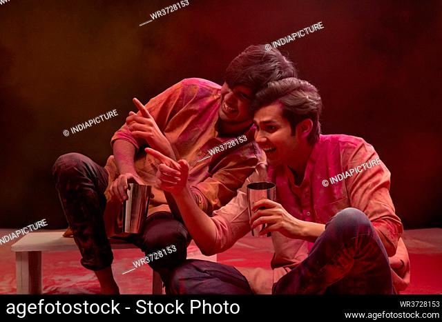 TWO YOUNG MEN HAPPILY POINTING AWAY WHILE DRINKING BHANG ON HOLI