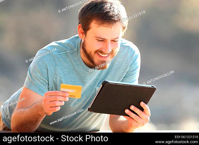 Happy man buying online with credit card and tablet outdoors