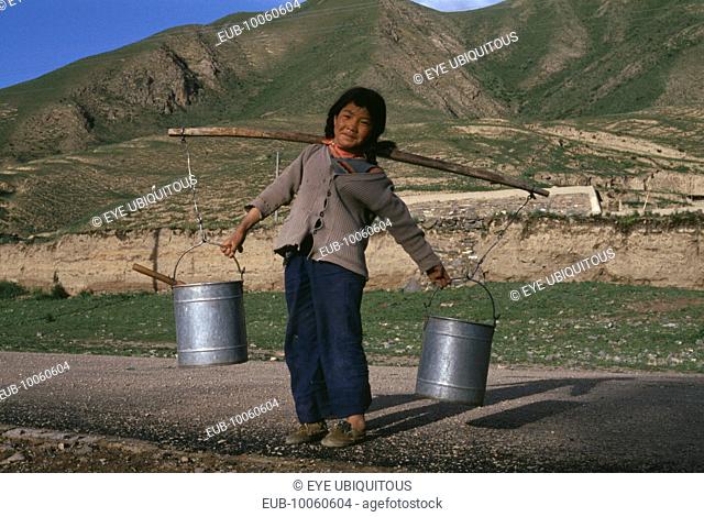 Child carrying water buckets on the ends of a stick over sholders
