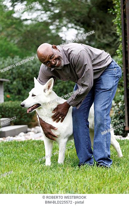 Black man petting white dog in backyard