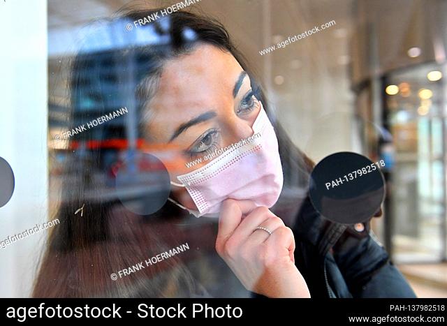 Topic picture Corona: A young woman with protective mask, face mask, community mask looks worried out of a window | usage worldwide