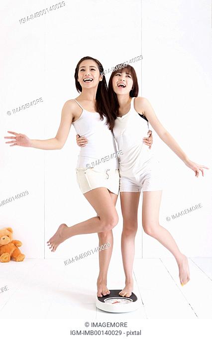 Young women standing with one leg on weight scale and looking up with smile