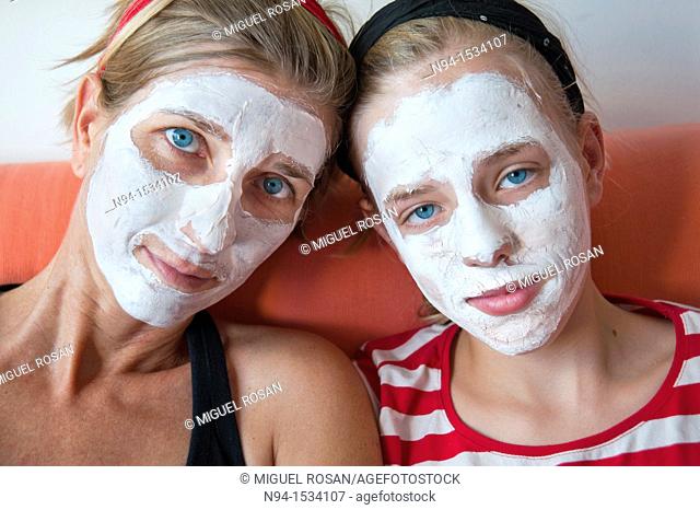 Young mother with her daughter at the time of relaxation  Using the free time for personal care  Using a facial mask to clean skin of the face
