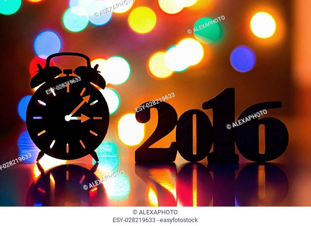 Silhouette of alarm clock and inscription of 2016 year with garland lights on background