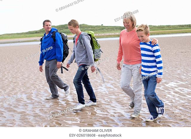 Family of four walking across the beach. They are wearing warm casual clothing with backpacks and look very happy