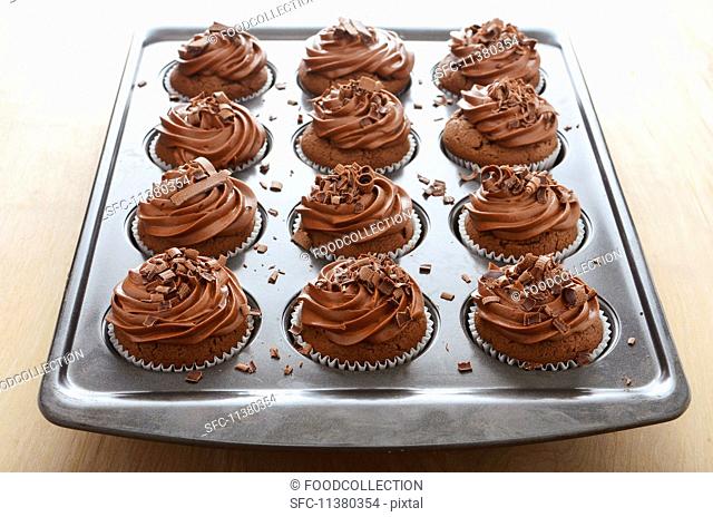 Chocolate cupcakes with butter cream and chocolate curls in a baking tin
