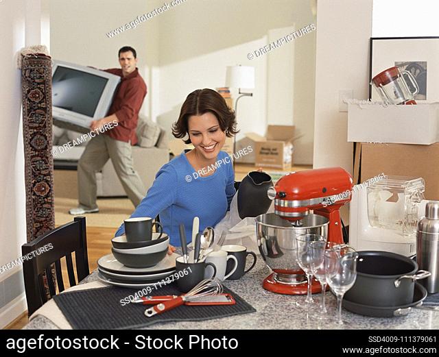 Young woman admiring kitchenware while partner moves tv