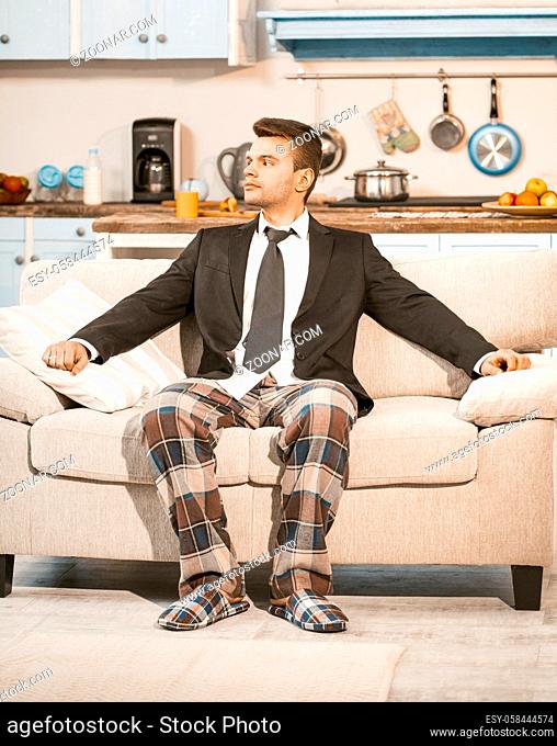 Bored Businessman Awaiting Quarantine Ending At Home, Serious Caucasian Man In Elegance Business Jacket And Pajama Pants Sits On Sofa Looking At Window
