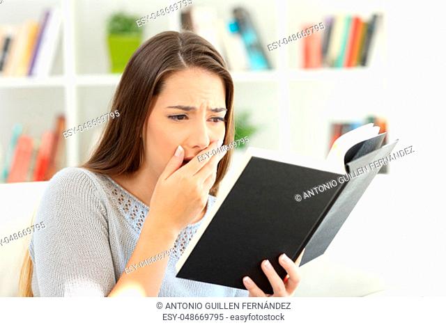 Worried woman reading a good drama book sitting on a sofa at home