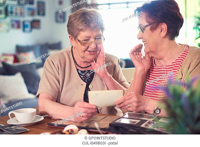 Two senior women chatting while looking at old photographs at table