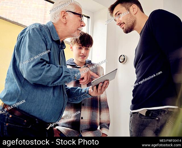 Son, father and grandfather looking at smart thermostat control on digital tablet at home