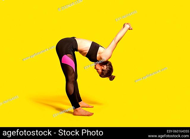 Athletic girl with hair bun in tight sportswear doing sport, bending and stretching hands backwards, warming up training muscles for flexibility
