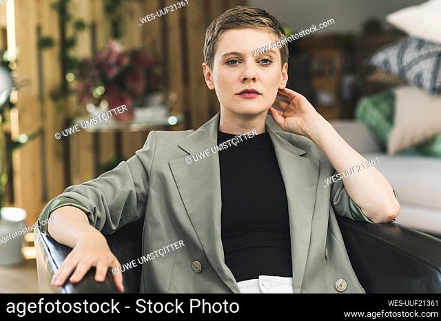 Confident businesswoman wearing blazer sitting on armchair at home