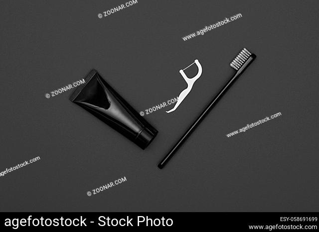 Close up one black toothpaste tube, floss and toothbrush over dark grey background, masculine dental care flat lay, elevated top view, directly above