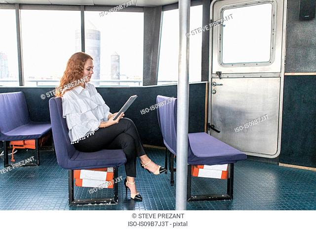 Stylish young businesswoman looking at digital tablet on passenger ferry