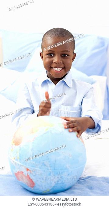 Smiling little boy holding a terrestrial globe lying on his bed