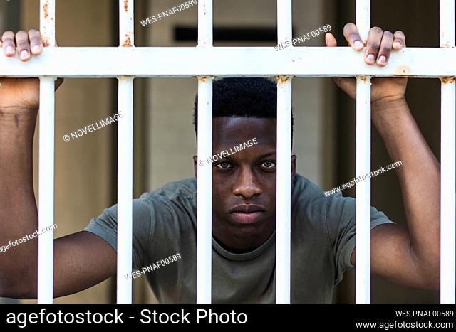 Young man looking through rusty metallic fence