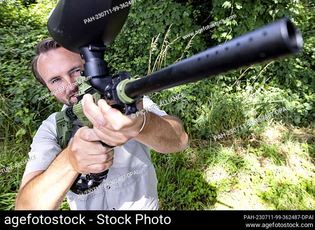 11 July 2023, North Rhine-Westphalia, Saerbeck: Ole Theisinger, a research assistant at Wald und Holz NRW, aims his paintball rifle at a web of oak...