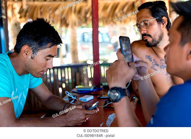Friends using smartphone in beach hut, Pagudpud, Ilocos Norte, Philippines