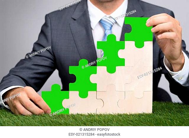 Businessman Holding Jigsaw Graph On Grass