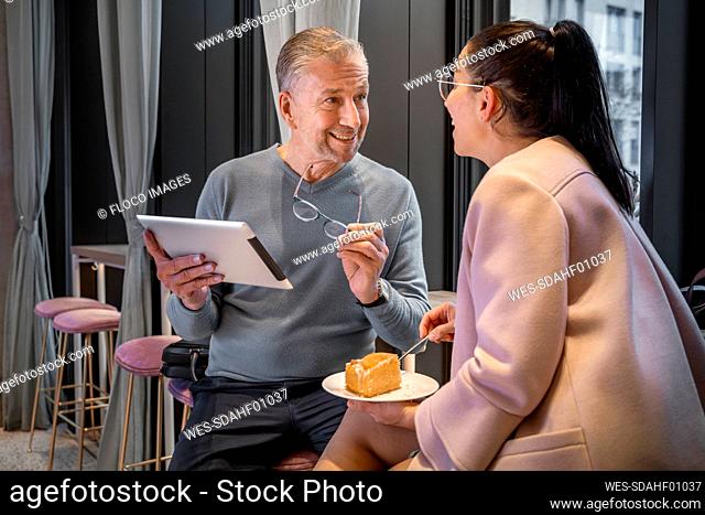 Businessman using digital tablet while sitting by colleague eating food at modern cafe