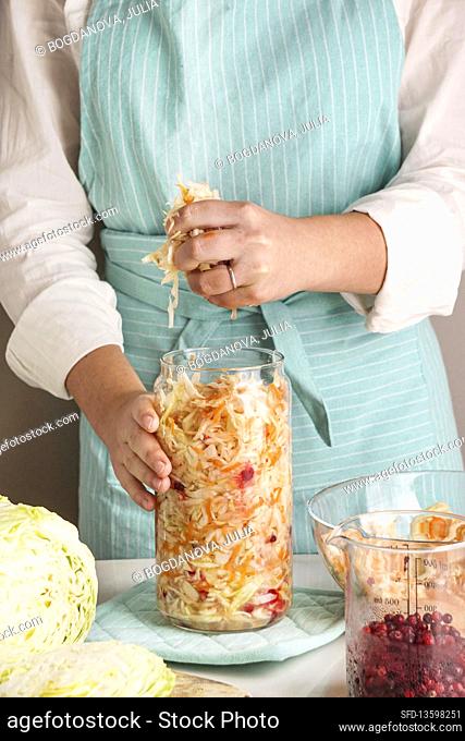 Cabbage fermented - woman packing into glass jar on table in kitchen