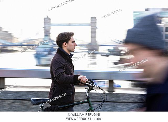 UK, London, businessman pushing bicycle in the city