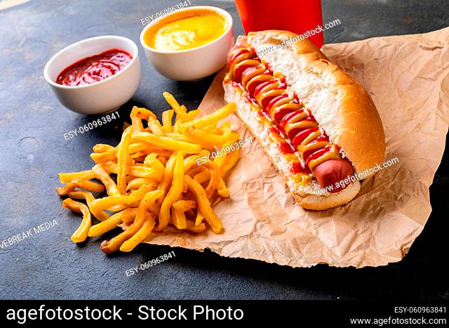 Hot dog with french fries and sauces on wax paper at table